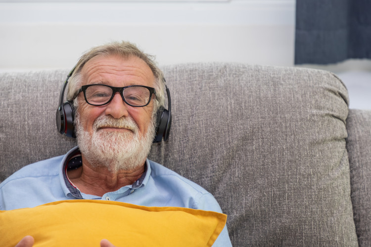 Älterer Herr mit Kopfhörern im Sofa